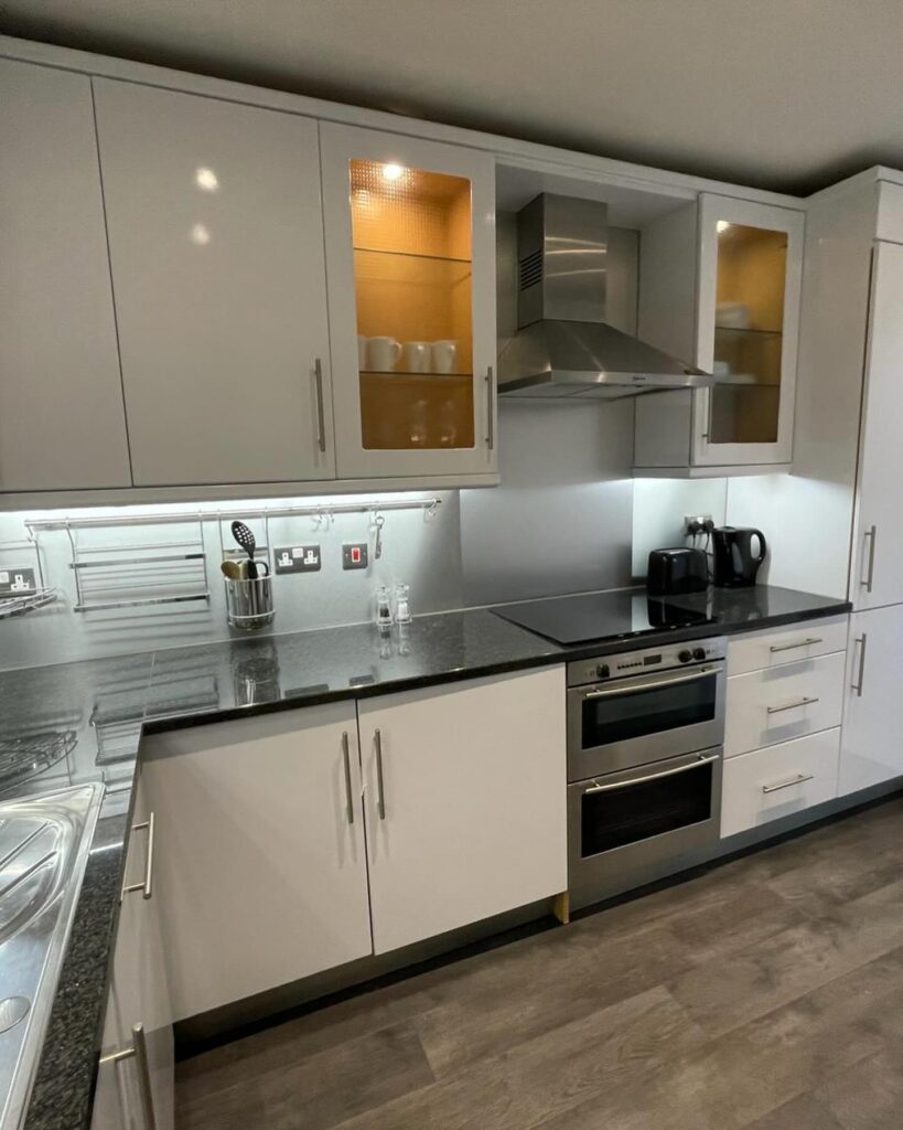 Side-by-side comparison of a kitchen's transformation in London with before image displaying outdated, beige cabinets and after image showcasing modern, white high-gloss vinyl wrapped cabinets.